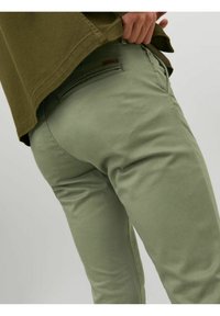 Pantalons en twill de coton vert clair à coupe slim avec taille mi-haute, poches latérales et arrière, et un subtil détail de couture près de la taille.