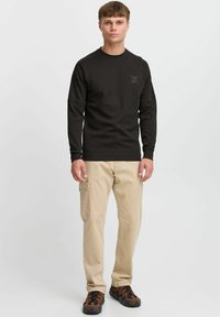Black long-sleeve sweatshirt with a crew neckline and logo detail. Paired with beige cargo pants and brown patterned sneakers.