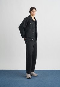 Black denim jacket with button closures, paired with matching black jeans. Gray sneakers complete the outfit. Simple, contemporary design.