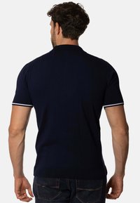 Camiseta polo de manga corta en color navy con rayas en el cuello y un diseño texturizado. Combinada con jeans de color azul oscuro, mostrando la vista trasera.