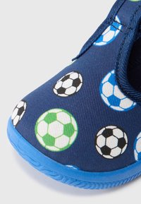 Modri slip-on čevelj z vzorcem nogometne žoge. Ima gornji del iz mornarsko modrega blaga, gumijast podplat ter pisane potiskane nogometne žoge v zeleni, črni in modri barvi.