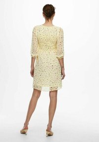 Keltainen kukkamekko, jossa on puffihihat, läpinäkyvä kangas ja rypytetty selkä. Pituus ulottuu puoliväliin reittä, ja siinä on kevyt, väljä muotoilu.