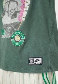 Groene katoenen t-shirt met basketbalgrafieken, een cirkelvormig "Nike Sports 1972" logo en een label met het Nike Swoosh ontwerp.