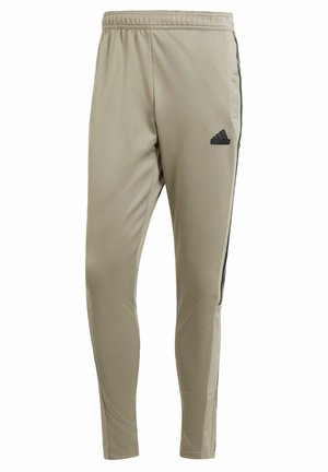 Light khaki athletic pants with a tapered fit, elastic waistband, side pockets, and black stripe accents. Features an embroidered logo on the thigh.
