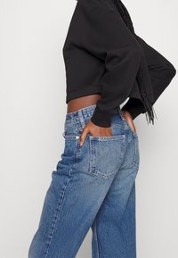 Black cropped sweatshirt with wide sleeves, paired with high-waisted light blue jeans featuring a classic five-pocket design and slight distressing.