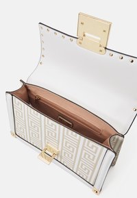 Sac à main structuré blanc et or avec un motif géométrique embossé, comportant un fermoir en or, ouvert avec un intérieur marron et une poche zippée.