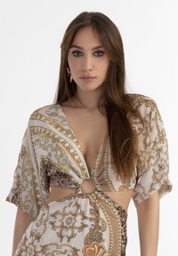 Ausschnittbluse mit kurzen Ärmeln, die mit einem beigen, goldenen und animalischen Druckmuster versehen ist. Knoten-Detail an der Taille, glatter, leichter Stoff.
