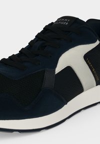 Черно-бяла маратонка Tommy Hilfiger с черни връзки и мрежест страничен панел, с брандирани детайли на езика и страната.