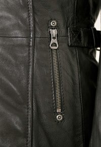 Close-up of a black leather jacket pocket with a closed silver zipper and a stitched leather strap detail beside it.