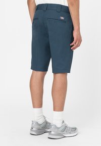 Pantaloni corti blu navy in tessuto liscio, con vita aderente, quattro tasche e una piccola etichetta con il marchio sul retro.