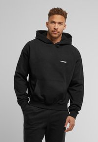 Black hoodie made of cotton with a front pouch pocket and drawstring hood. Features a small white logo on the chest and ribbed cuffs.