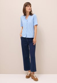 Helles blaues Kurzarmhemd, kombiniert mit dunkelblauen weitgeschnittenen Jeans und braunen Sneakers. Glatte Textur, lässiges Design.