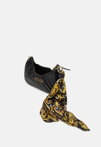 Prošívaná černá kabelka se zlatým kováním a ozdobným černo-zlatým šátkem přivázaným na popruhu. Horní část uzavíratelná zipem.