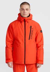 Veste isolante rouge avec fermeture éclair sur le devant, capuche ajustable et poignets élastiques. Comprend une poche poitrine zippée et un détail de logo.