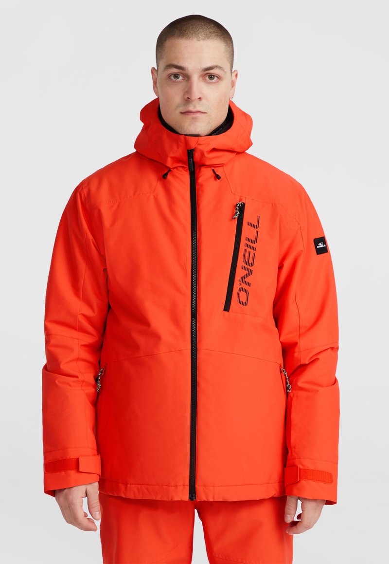 Veste isolante rouge avec fermeture éclair sur le devant, capuche ajustable et poignets élastiques. Comprend une poche poitrine zippée et un détail de logo.