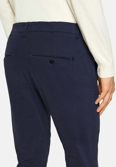Pantalon navy avec une texture lisse, doté d'une poche arrière avec fermeture à bouton. Le tissu semble léger et bien coupé.