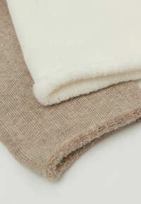 Dwa złożone kawałki materiału: jeden biały o żeberkowanej teksturze, drugi jasnobrązowy o gładkim wykończeniu. Oba mają miękkie, wykończone krawędzie.