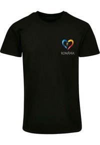 Juodas medvilnės marškinėlis su širdies dizainu mėlyna, geltona ir raudona spalvomis, o po logotipu kairėje krūtinės pusėje yra tekstas "ROMÂNIA".