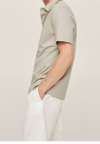 Pánská polokošile s krátkým rukávem ve světle šedé barvě s límečkem, doplněná bílými kalhotami. Má volný střih a minimalistický design.