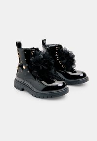 Czarne lakierowane botki za kostkę z złotymi ćwiekami w kształcie serca, czarne koronkowe akcenty w kwiaty, sznurowany design i teksturowana gumowa podeszwa.