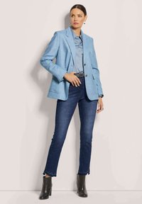 Helles blauer maßgeschneiderter Blazer über einem hellblauen Hemd, kombiniert mit dunklen Jeans und schwarzen Stiefeletten, mit einem eleganten Design und minimalen Akzenten.