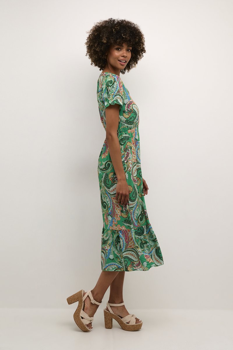 Green paisley-patterned dress with short sleeves, fitted waist, and flared hem. Paired with tan platform heels made of woven material.