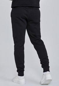 Zwarte sweatpants met een tapered fit, gemaakt van zacht materiaal. Heeft een elastische tailleband en geribde boorden. G gedragen met witte sneakers.