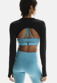 Sort langærmet top med åben ryg, parret med en blå sports-bh med krydssnore, og matchende blå højtaljede leggings.