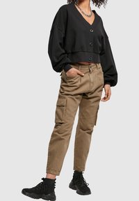 Black cropped sweater with button closure and wide sleeves, paired with khaki cargo pants featuring side pockets and a relaxed fit. Black shoes.