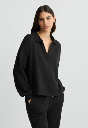 Sweat-shirt polo noir à manches longues avec un col en V et une coupe décontractée. Présente des accents texturés et des poches latérales pour un design pratique.