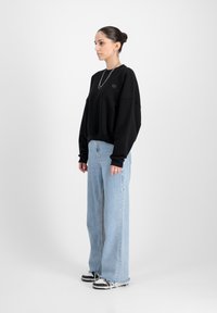 Felpa nera oversize con logo frontale, abbinata a jeans a gamba larga di colore blu chiaro. Il look è completato da sneaker bianche e nere.