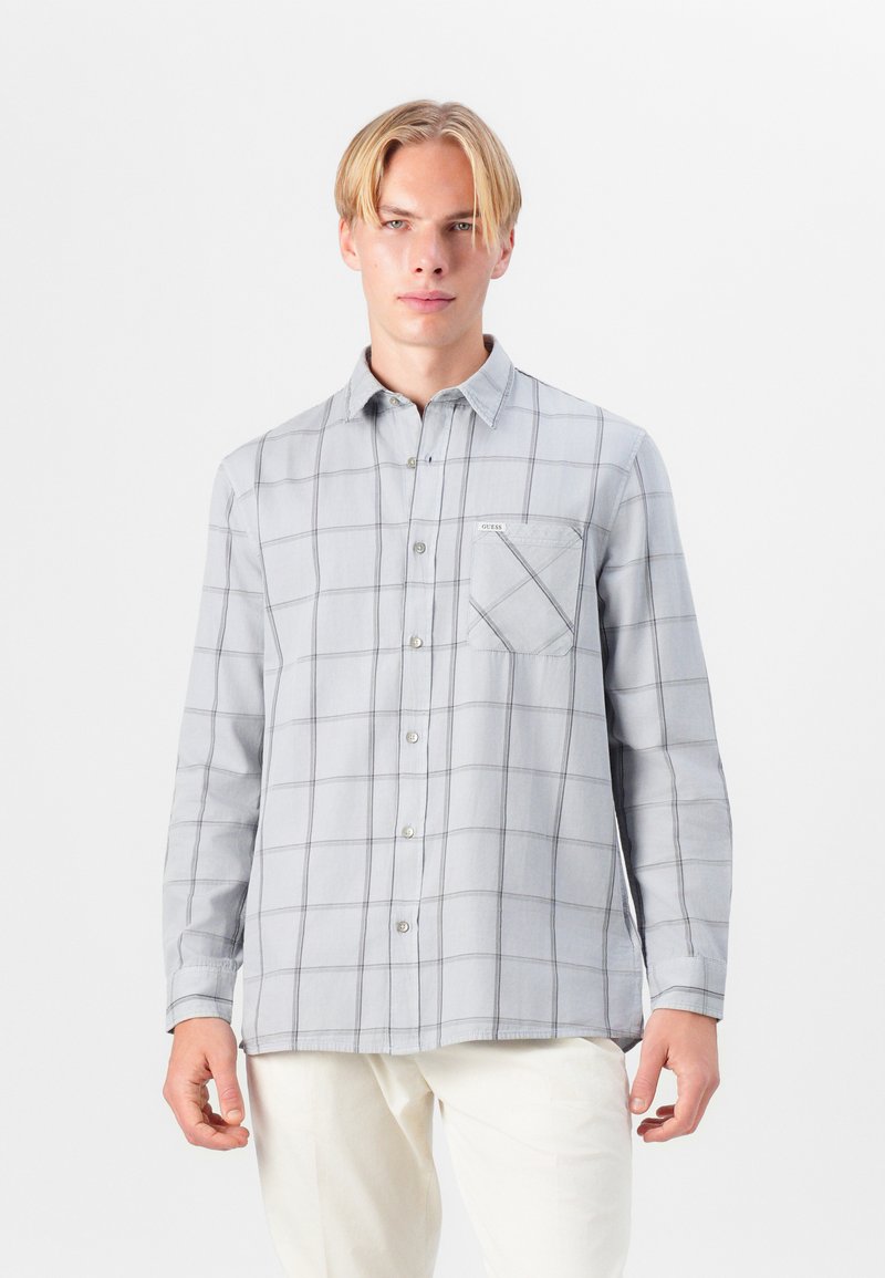 Camisa de botones gris claro con un patrón de cuadros, con un bolsillo en el pecho y mangas largas. Hecha de una tela suave, con costuras detalladas visibles.