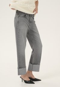 Jeans de mezclilla gris con un ajuste ligeramente holgado, con puños deshilachados, bolsillos laterales y un diseño clásico de cinco bolsillos. Llevados con mules de tacón negro.