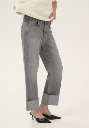 Gray denim jeans with a slightly loose fit, featuring frayed cuffs, side pockets, and a classic five-pocket design. Worn with black heeled mules.