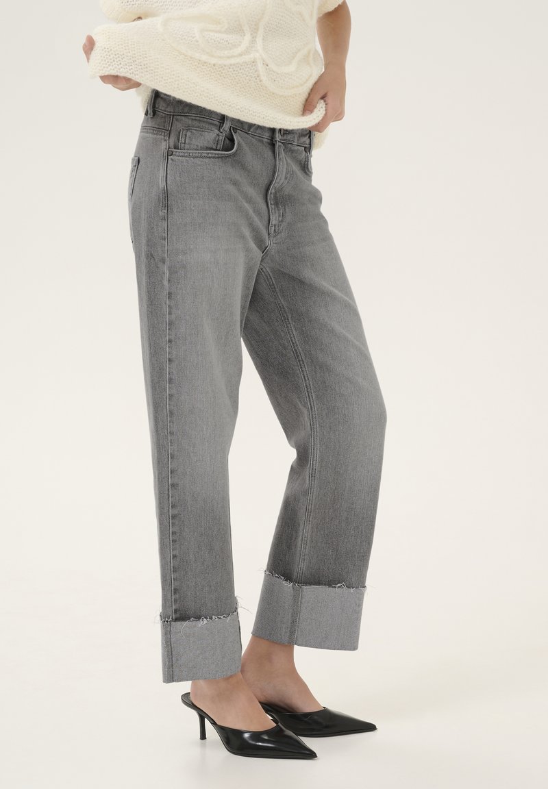 Jeans de mezclilla gris con un ajuste ligeramente holgado, con puños deshilachados, bolsillos laterales y un diseño clásico de cinco bolsillos. Llevados con mules de tacón negro.