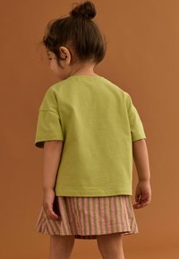 T-shirt verde in cotone con maniche corte, abbinato a una gonna plissettata con strisce verticali rosa e bianche. Stile semplice e casual.