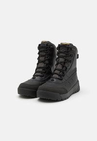 Schwarze wasserdichte Stiefel mit einem hohen Knöcheldesign, strukturiertem synthetischem Obermaterial, verstärkter Zehenkappe und dicker Gummisohle mit Gripmustern.