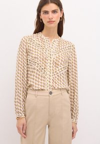 Blusa a maniche lunghe color crema con un motivo floreale in rosa e verde. Presenta una chiusura con bottoni sul davanti e dettagli arricciati lungo le spalle.