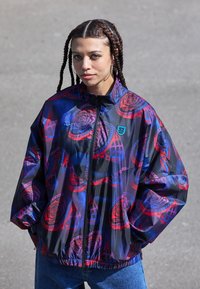 Colorful windbreaker with abstract rose patterns in red and blue on a dark background. Features a high collar and zip closure.