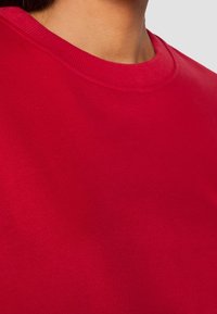 Felpa rossa in cotone con collo a giro e bordo a coste, caratterizzata da una texture morbida e un colore uniforme e liscio.