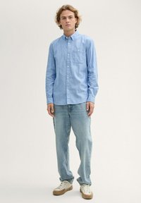 Hellblaues Button-up-Hemd mit einer Brusttasche, kombiniert mit hellblauen, locker sitzenden Jeans und cremefarbenen Sneakers.