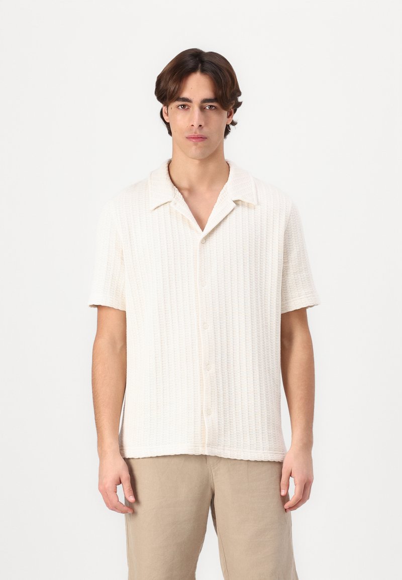 Kortärmad, knappad skjorta i off-white, texturerad tyg med krage. Har vertikal ribbad mönster och mjukt, lättviktsmaterial.