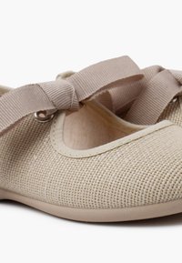 Bailarinas de malla beige con superficie texturizada, que cuentan con un lazo de cinta en el empeine y una suela flexible de goma.