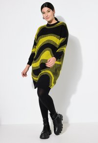 Maglione oversized a righe verdi e nere con scollatura rotonda, polsini a costine e design morbido, abbinato a leggings neri e stivali chunky.