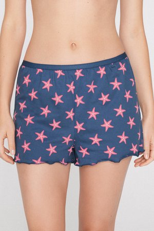 Pantalones cortos azul marino con estampado de estrellas de mar rosas, usados por una persona con el abdomen descubierto, mostrando cinturilla elástica y bordes con volantes.