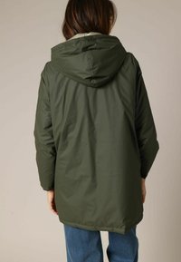 Veste verte à capuche en matériau résistant à l'eau. Dotée d'une coupe décontractée et d'un design simple avec un ourlet arrière plus long.