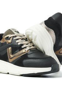 Schwarze und goldene Sneakers bestehen aus einer Kombination von Leder und Mesh-Materialien, haben eine strukturierte Oberfläche und eine robuste weiße Sohle mit ausgeprägtem Profil.