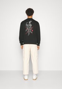 Felpa nera con design grafico sul retro, polsini e orlo a coste. Abbinata a pantaloni cargo beige chiaro e sneakers bianche.