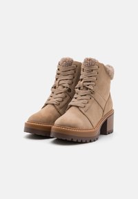 Botines de ante marrón con un borde de piel de textura suave, punta redonda y diseño con cordones. La suela de goma robusta y el tacón ancho ofrecen estabilidad.