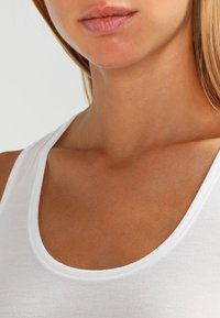 Witte tanktop met een ronde halslijn, gemaakt van gladde, lichte stof. Schone stiksels langs de randen.